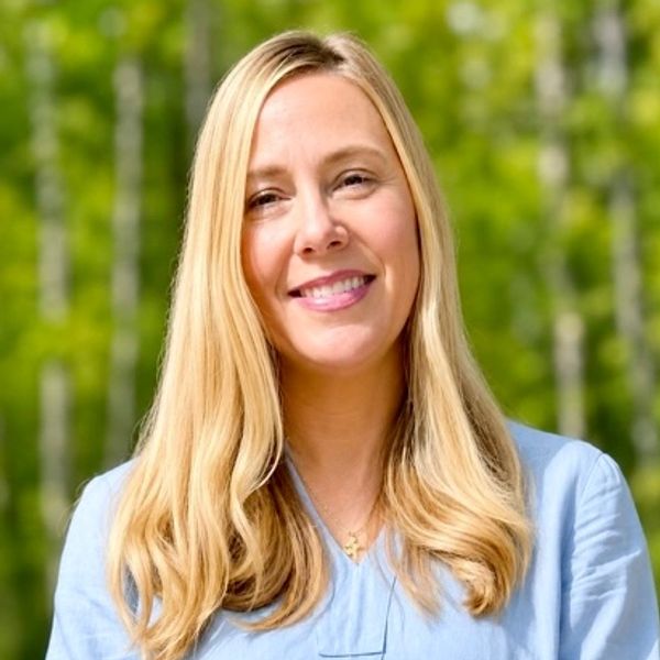 Smiling woman with long blonde hair outdoors in a blue shirt.