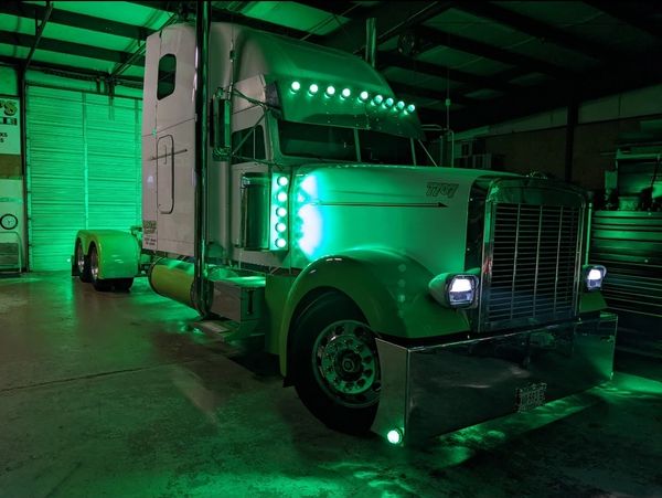 A semi-truck with its lights on, parked at night.