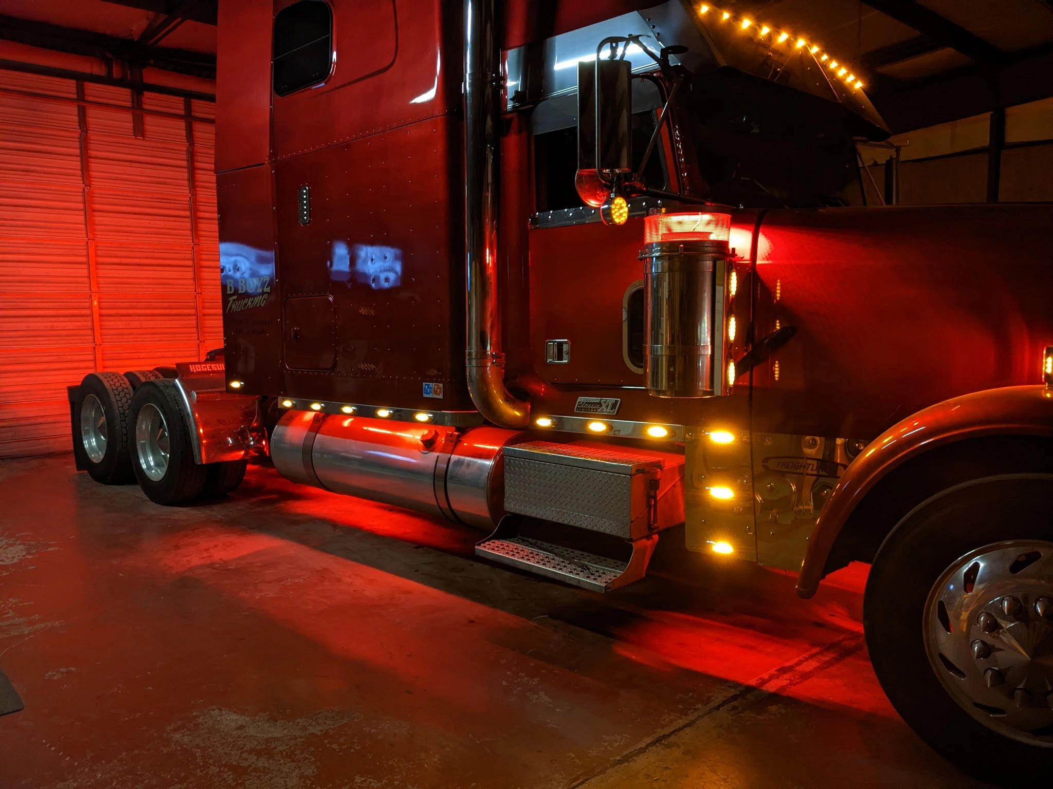 A semi-truck with its lights on, parked at night.