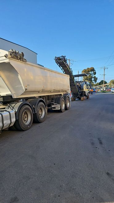 A semi tipper being loaded by an asphalt profiler on a road construction job.