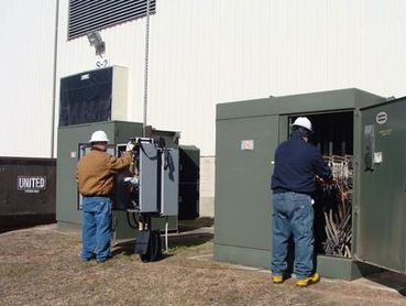 Technicians inspecting large outdoor transformer.
