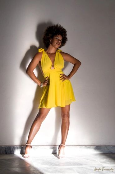 Woman poses confidently in a bright yellow dress against a plain wall.