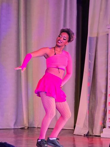 Dancer in bright pink outfit performing on stage with confident smile.