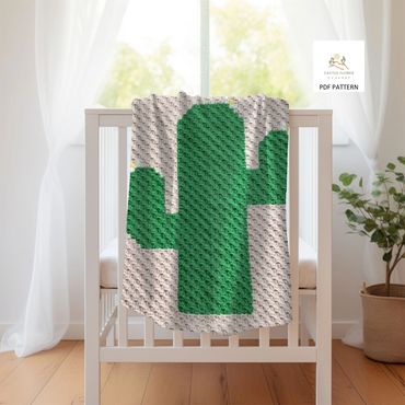 Baby blanket with a large green saguaro on a tan background, draped over a crib
