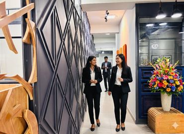 Two women in black suits walking and talking in a modern office hallway.