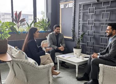 Three professionals having a discussion in a modern office lounge with plants.