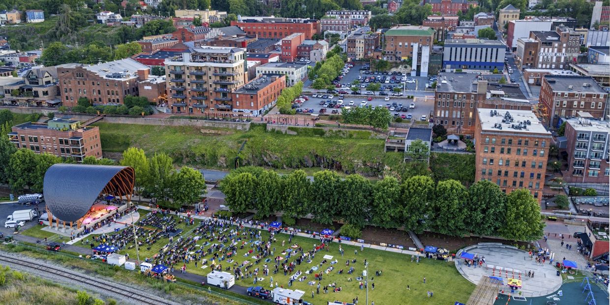 Outdoor concert with a wooden stage and seated audience in an urban park.