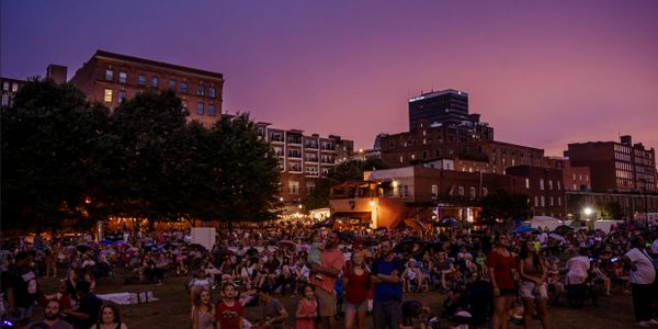 Crowd gathered at an outdoor evening event in an urban park.