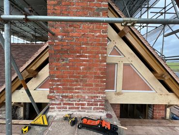Construction tools on a rooftop near a brick chimney and wooden framing.