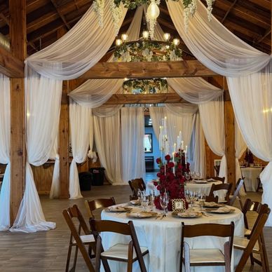 Elegant wedding reception setup with draped white fabric and floral centerpieces.
