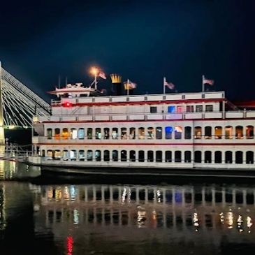 A brightly lit riverboat at night with reflections on the water.