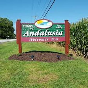 Welcome sign for the Village of Andalusia beside a road and cornfield.