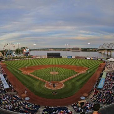 A baseball stadium with a ferris wheel and river in the background under a cloudy sky.