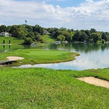 Scenic golf course with water hazard and lush greenery under a blue sky.