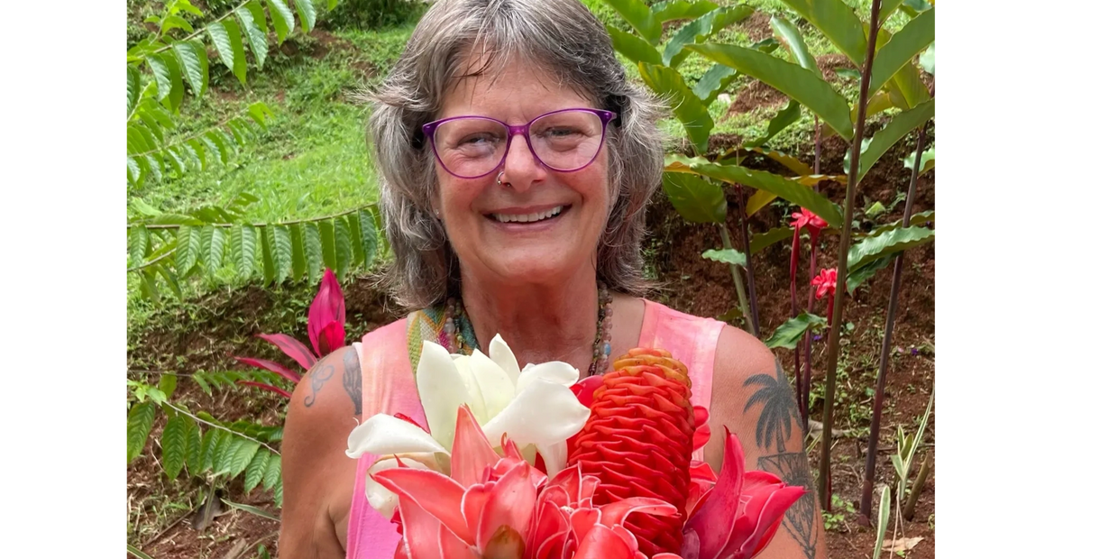 Smiling woman with purple glasses holding a vibrant bouquet of tropical flowers.