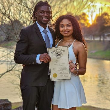 Couple proudly holding their marriage license outdoors at sunset.