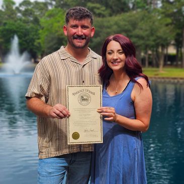 Couple holding a marriage license near a water fountain.