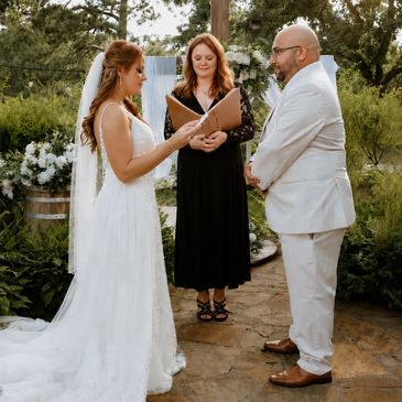 Bride and groom exchanging vows outdoors with officiant.