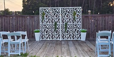 Outdoor wedding setup with white chairs and decorative backdrop.