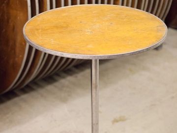 Round wooden table with a single metal leg in a storage area.