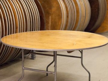 Round wooden table with metal legs in a storage area.
