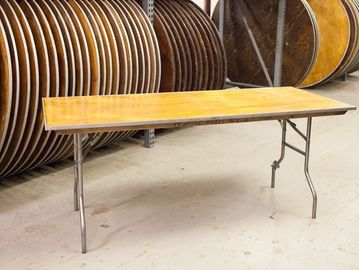 A wooden folding table with metal legs in a storage area.