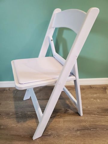 White folding chair with cushion against a teal wall on wooden floor.