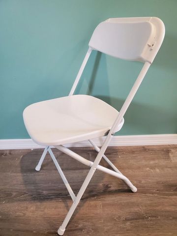 White folding chair against a blue wall on wooden floor.