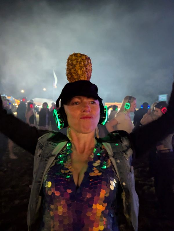 Woman wearing headphones and a pineapple on her head at a nighttime outdoor event.