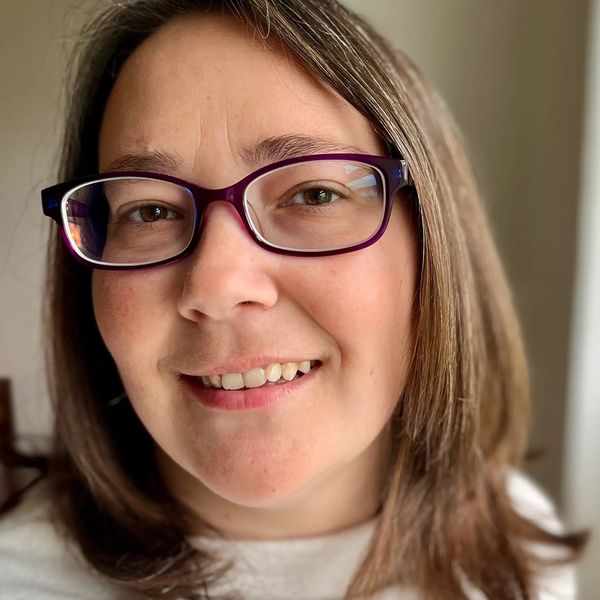 Close-up of a smiling woman with glasses and shoulder-length hair.