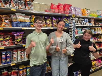 Three people giving thumbs up in a snack aisle.