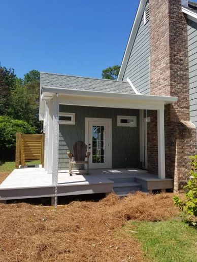 Small covered porch with chair, attached to gray house with brick chimney.