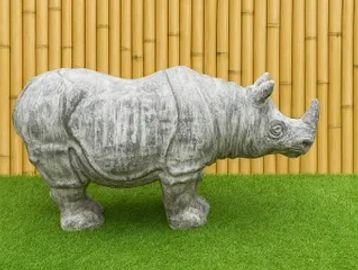 A gray rhino statue stands on green grass against a bamboo fence.