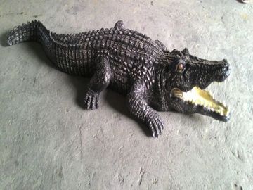 A realistic crocodile sculpture on a concrete floor with a person's feet visible.