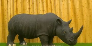 A realistic black rhinoceros statue on green grass with a bamboo background.
