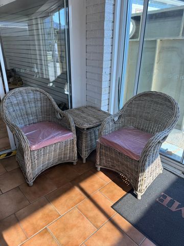 Two wicker chairs with cushions and a matching wicker table on a tiled floor.