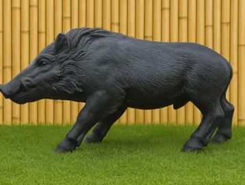 Black wild boar statue on green grass in front of bamboo fence.