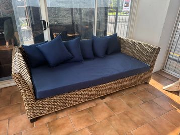 Wicker sofa with navy blue cushions on a tiled floor.