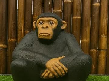 Sculpture of a contemplative chimpanzee sitting on green grass with a bamboo backdrop.