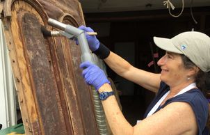 Woman cleaning an antique door with a brush and vacuum