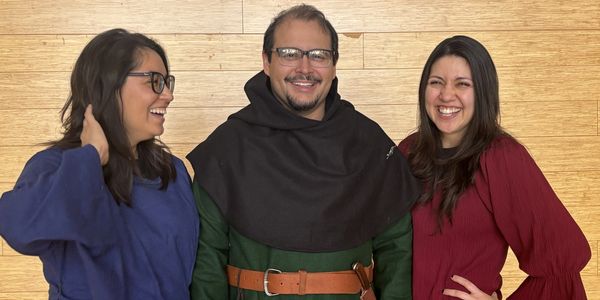 Three people smiling and posing against a wooden wall.