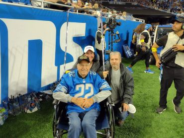 An elderly man in a wheelchair at a sports event with two companions.