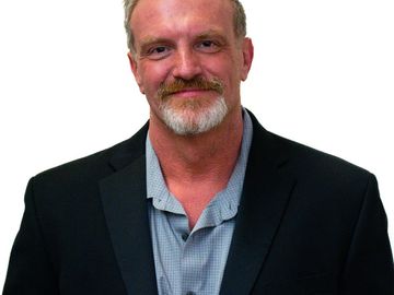 Smiling man with a beard in a blazer and shirt.