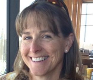 Smiling woman with brown hair and pearl earrings indoors at a restaurant.