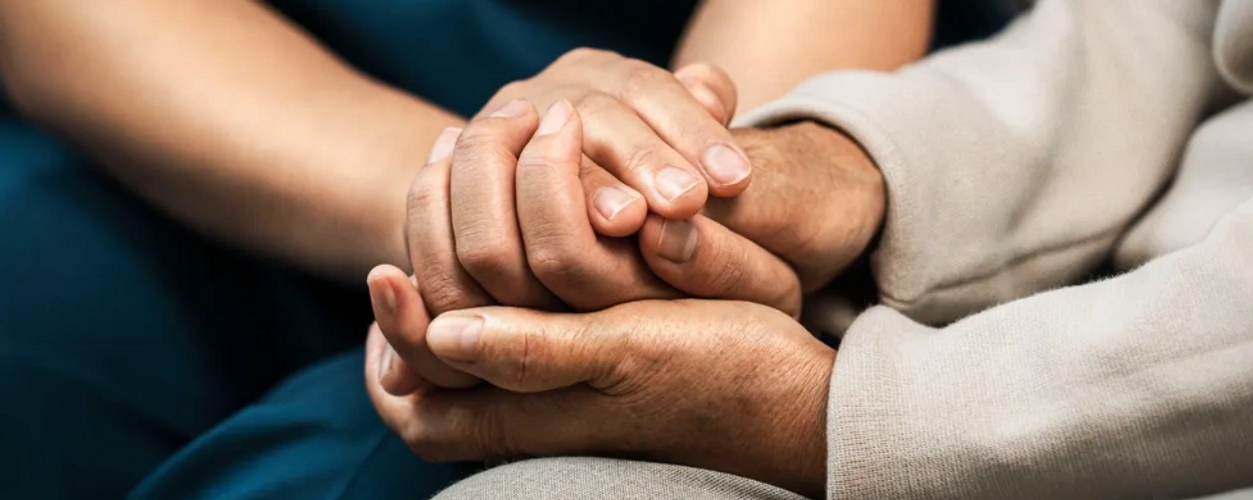 A healthcare professional comforting an elderly person by holding their hands.