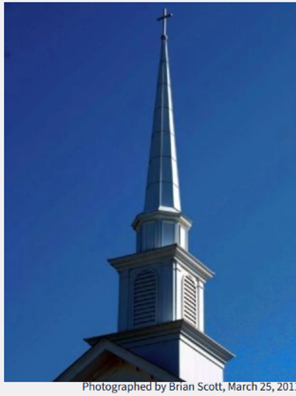 Tall white church steeple with a cross against a clear blue sky.