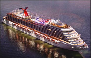 Illuminated Carnival Panorama cruise ship sailing in calm waters at dusk.