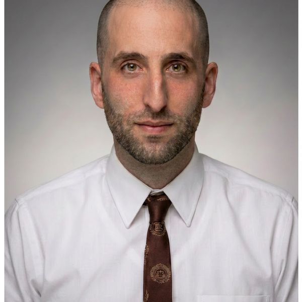 Professional portrait of a man in a white shirt and patterned brown tie.
