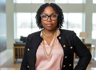 Confident woman in stylish professional attire stands with hand on hip indoors.