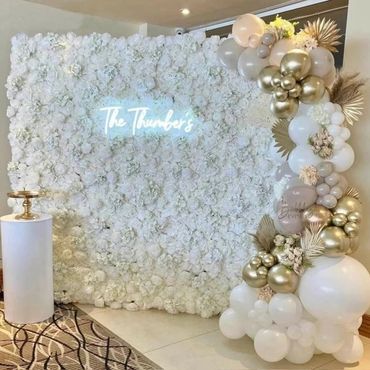 Elegant white floral wall with gold and white balloon decorations.